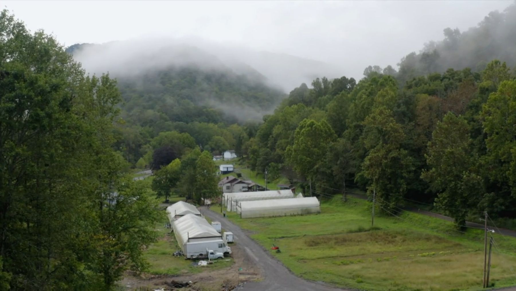 Aerial view of T&T high tunnels along a road in a misty, wooded Appalachian valley.