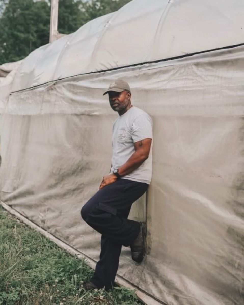 Jason Tartt, Sr. leaning against a high tunnel on the farm.